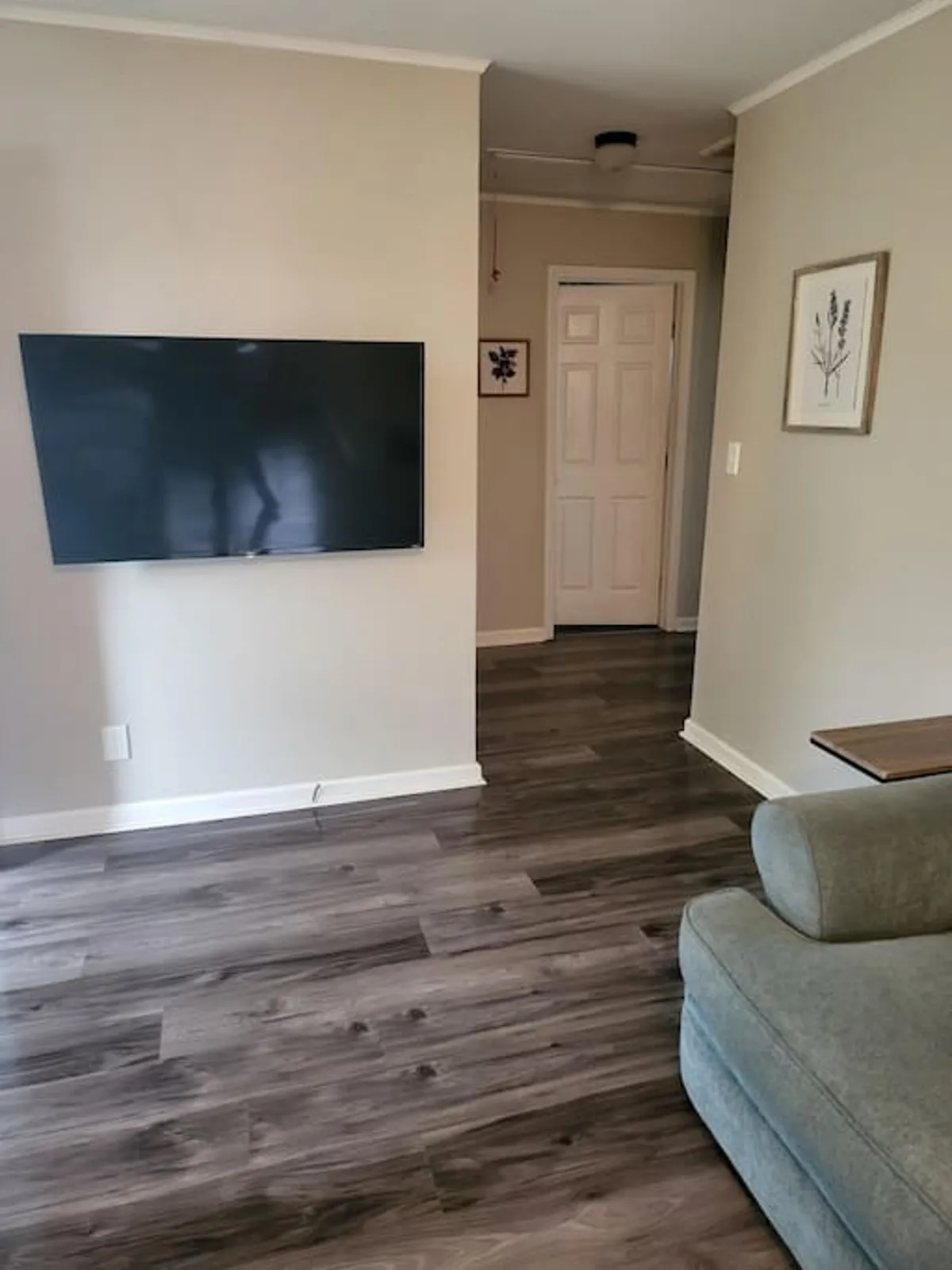 A comfortable living area featuring a plush sofa, a television, tasteful wall decor, and a doorway that hints at the open-plan layout. The setting is casual and inviting, with enough space for relaxing or entertaining guests, perfect for movie nights, game sessions, or quiet moments.