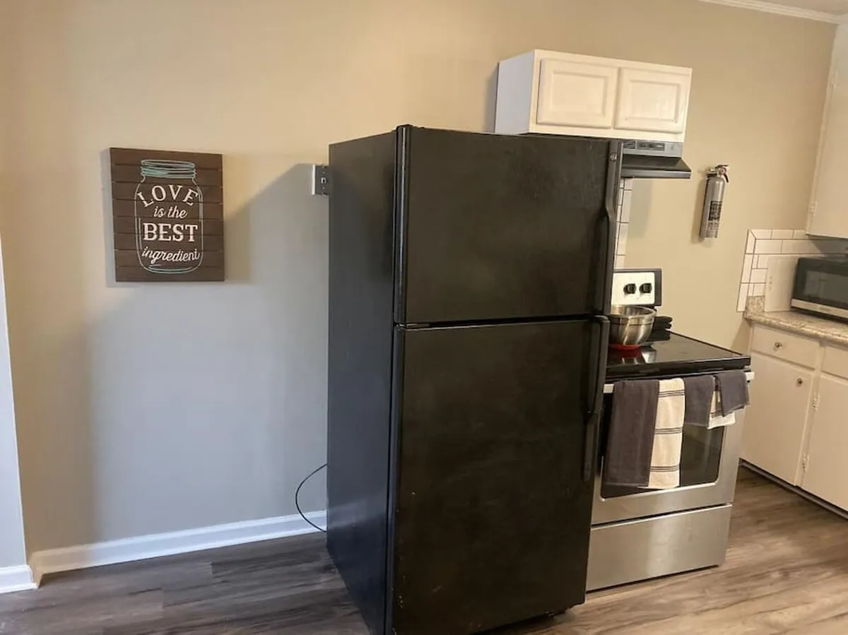 A kitchen view featuring a black refrigerator, a stainless steel stove, and wooden wall art, blending modern functionality with homely touches. The setup invites both meal preparation and family traditions, set in a warmly decorated environment.