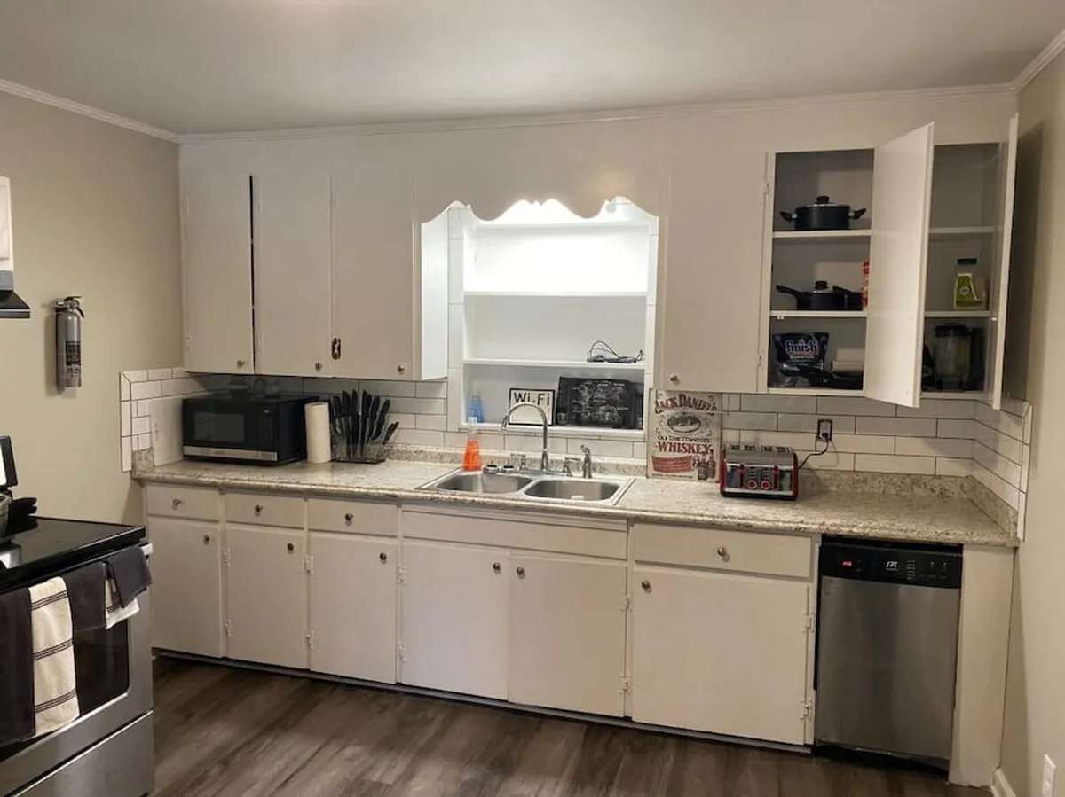 A view of the kitchen featuring a spacious countertop, modern microwave, stove, open cabinetry, and a sink. The layout is clearly organized for meal preparation and encourages both cooking and entertaining. The scene conveys a welcoming, functional space where multiple people can gather and interact.