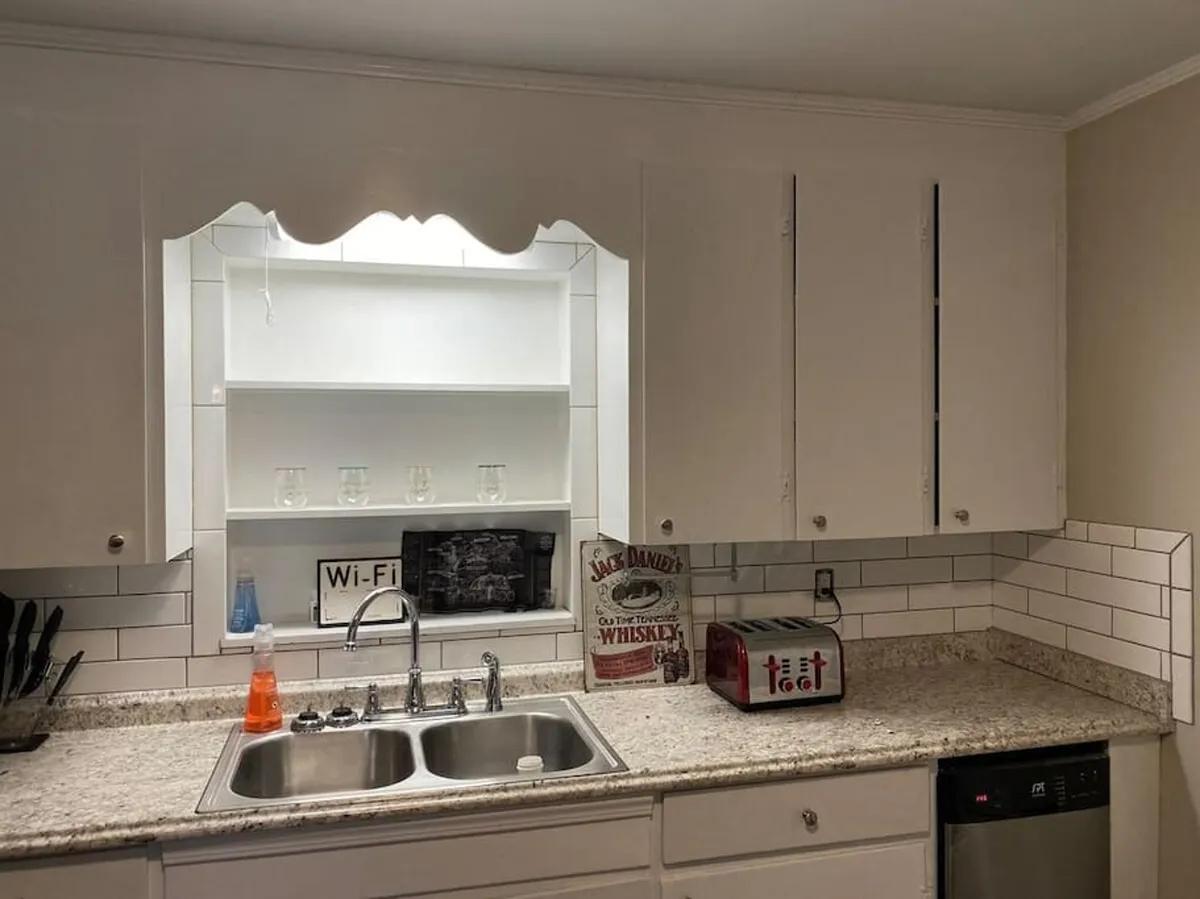 A bright, recently renovated kitchen area featuring a modern sink, clean kitchen cabinets, and a cozy toaster. A distinctive whiskey sign adds local Tennessee flair. The space feels inviting and functional, suitable for preparing meals before heading out or enjoying casual gatherings with friends.