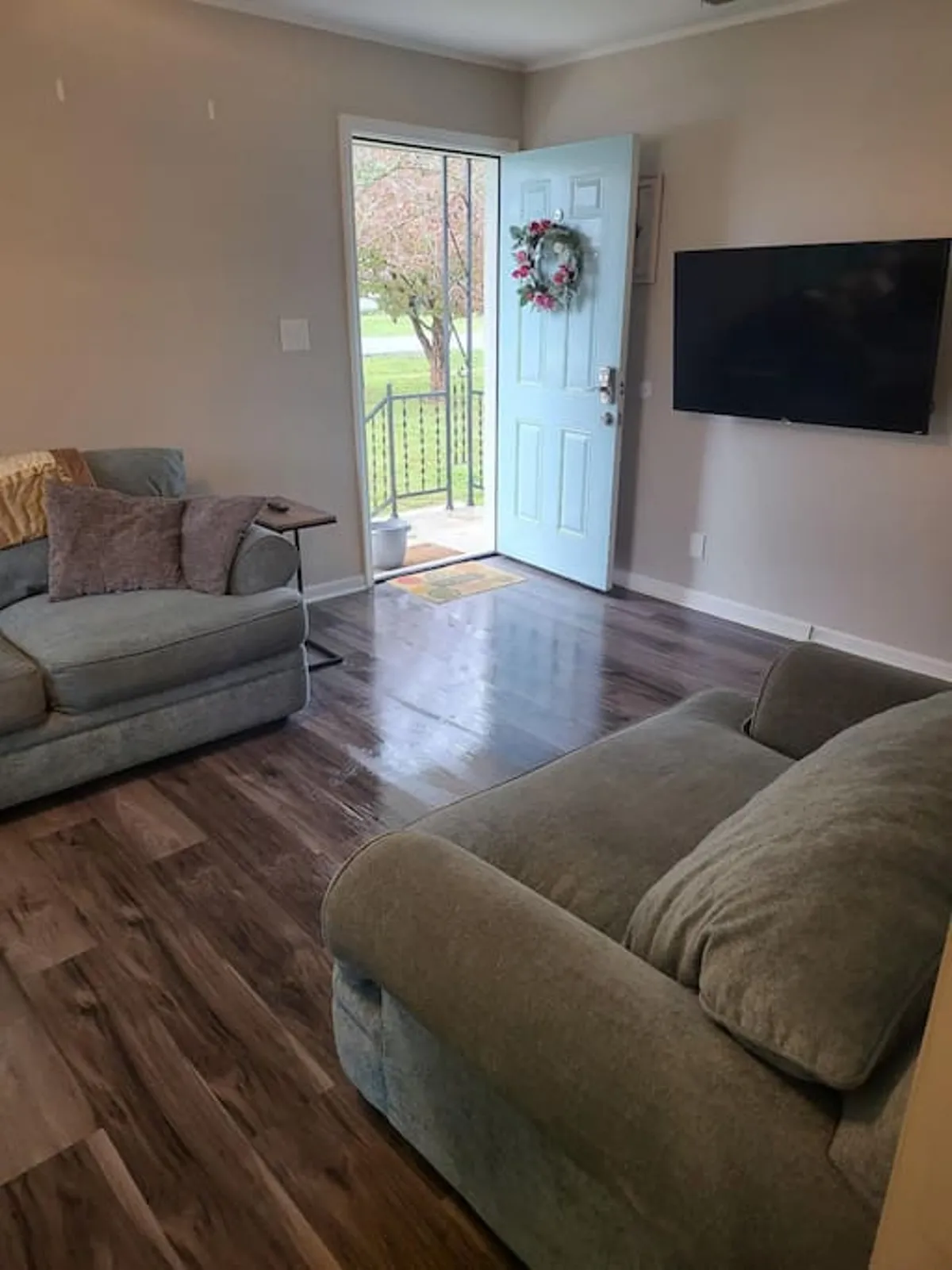 A welcoming living space with multiple sofas, a TV, an open door that brings in natural light, and a decorative wreath accentuating the homey ambiance. The layout is conducive to socializing, relaxation, and enjoying sunny afternoons.