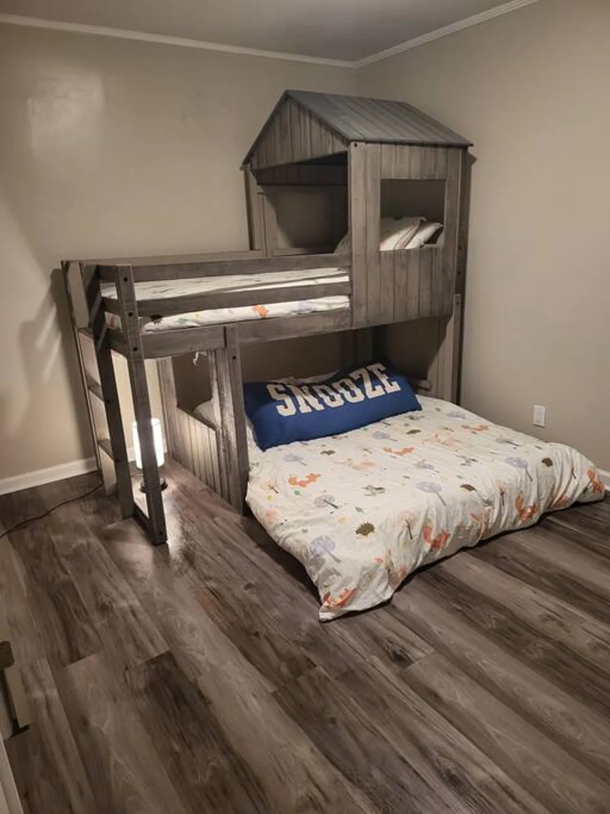 A playful kids' bedroom featuring a modern bunk bed and a floor mattress adorned with colorful, decorative pillows. The setup invites imaginative play and cozy sleepovers, making it a fun haven for younger guests.
