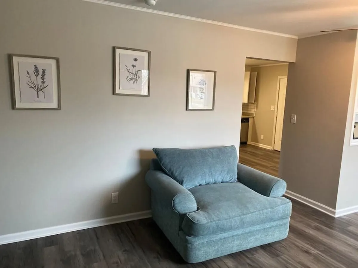 A sunlit sitting area with a comfortable blue armchair and framed botanical prints on neutral-colored walls, creating a tranquil and cozy atmosphere—ideal for unwinding after a busy day outdoors.