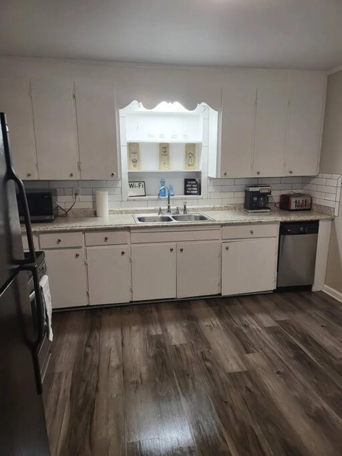 A well-lit, cozy kitchen featuring a sink, kitchen cabinets, a microwave, dishwasher, and a charming decorative shelf. The space feels family-friendly and functional, inviting guests to cook or gather for shared meals.